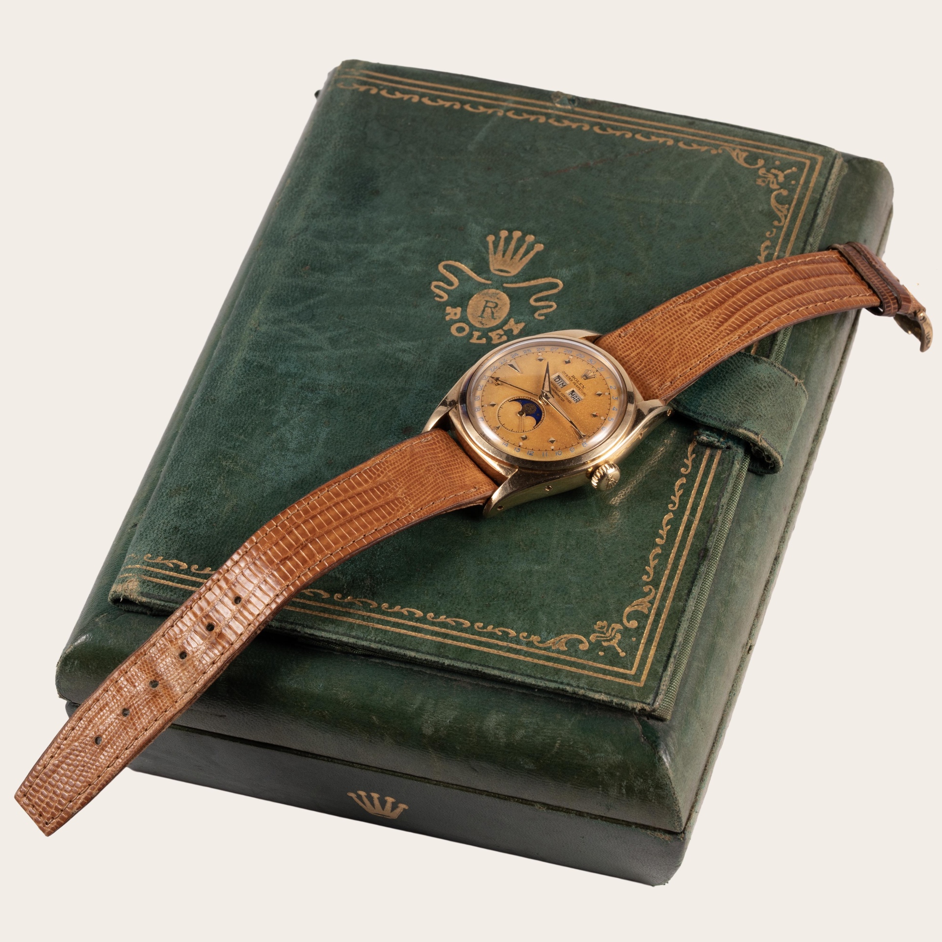 Vintage gold triple calendar moon phase wristwatch on a lizard strap resting on its green presentation box
